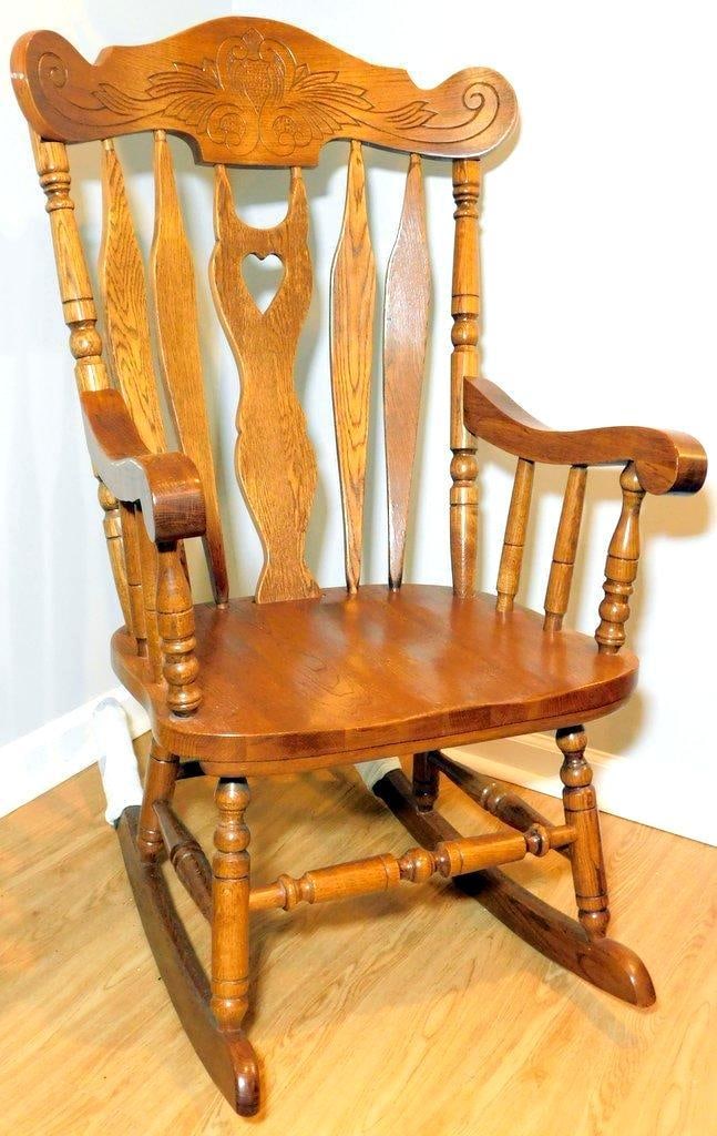 Carved Oak Rocking Chair w/ Heart Detail: Carved oak rocking chair featuring a decorative carved crest with intricate motifs, a central splat with heart cutout detail, and turned arm and leg supports The chair showcases a medium oak finish