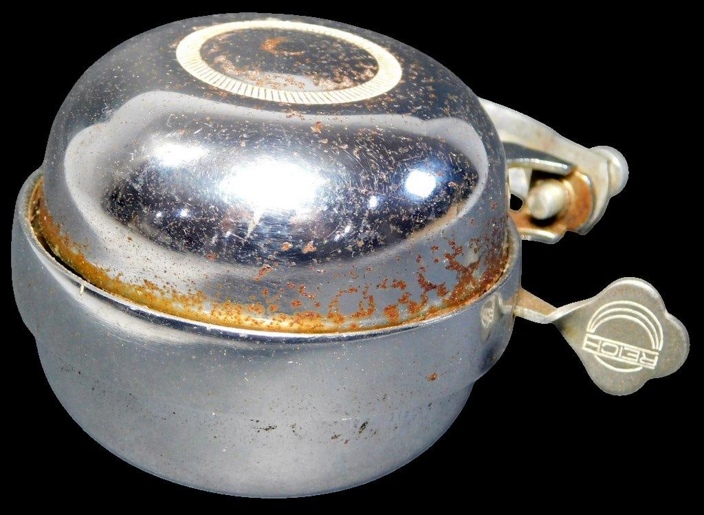 Vintage Reich Chrome Bicycle Bell: Reich chrome bicycle bell featuring a classic dome-shaped design with embossed detailing on the top The bell includes a stamped Reich logo on the lever and a metal mounting clamp for attachment