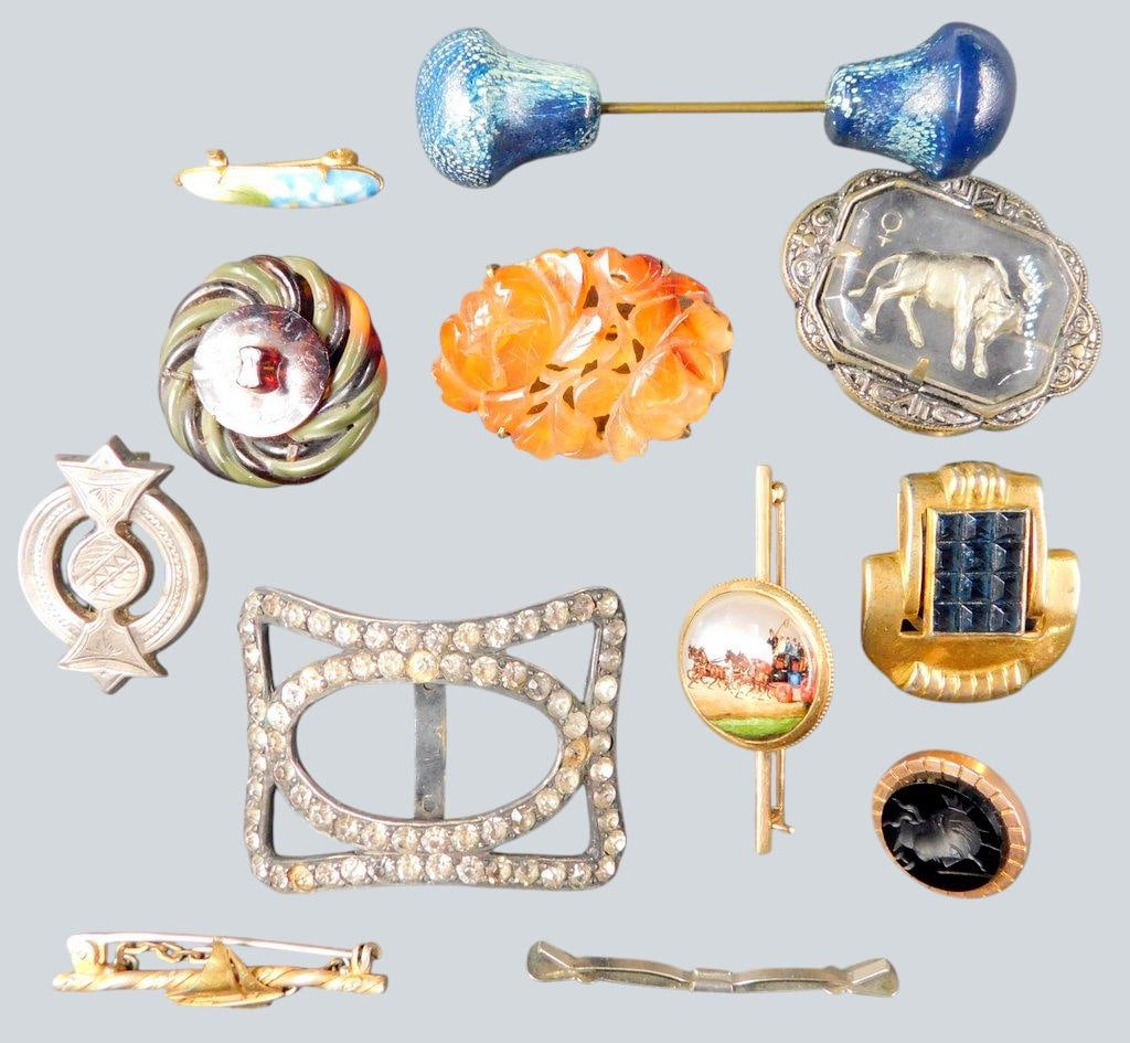 Grouping of Small Decorative Brooches and Accessories: A varied collection of decorative and vintage-style brooches, pins, and accessories featuring materials like metal, enamel, glass, and carved pieces Includes a rhinestone belt buckle, a painted scene