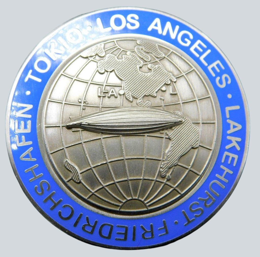 German WWII Zeppelin Air Ship Lakehurst Tokio Los Angeles Tour Badge: Two-piece die-struck vaulted nickel construction with blue enamel. Front shows the profile of a Zeppelin air ship flying over two world continents. Reads TOKIO - LOS ANGELES - LAKEHURST