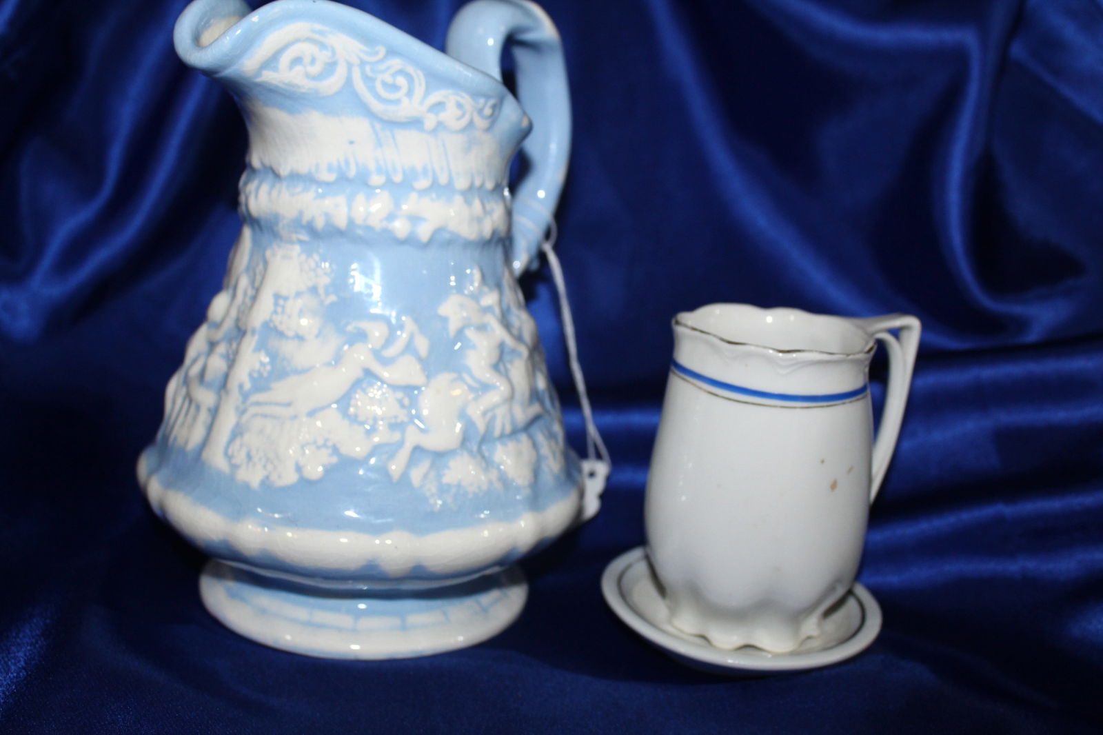 Lot of 2 Blue and White Ceramic Pitchers: 2 ceramic blue and white pitchers. One is small and comes on a tiny saucer, appears to have been part of a tea set at one time. The other is large, and appears to be hand thrown, hand painted, and dat