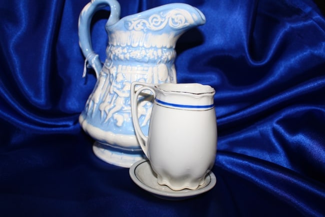 Lot of 2 Blue and White Ceramic Pitchers: 2 ceramic blue and white pitchers. One is small and comes on a tiny saucer, appears to have been part of a tea set at one time. The other is large, and appears to be hand thrown, hand painted, and dat