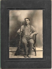 antique mounted photograph of a man seated with a rifle