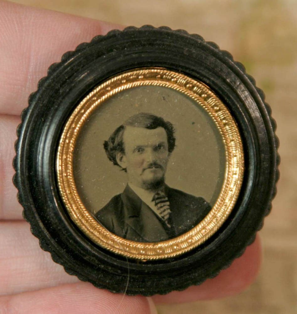 antique gutta percha frame with photograph: round black gutta percha frame with lid (damage/loss as shown) and star design and with very crisp antique portrait of a man in a suit and with hand tinted cheeks aprox 1 1/2" in diameter