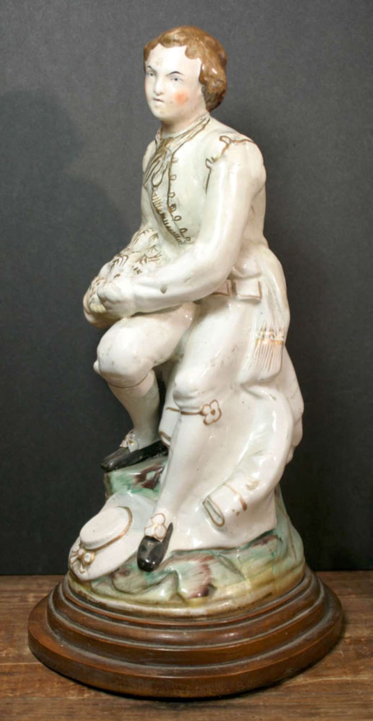 antique English pearlware figural statue: figural pearlware or paste statue of a gentleman in fancy clothing with gilt accents holding a basket of fruit or cookies, drilled and sitting on a wooden base to be wired as a lamp about 14 1/2