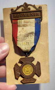 antique fireman badge or medal: badge or medal on a likely bronze pin brooch reading Souvenir and with red&comma; white and blue ribbon reading State Fireman&apos;s Association Philadelphia (illegible date/year)&comma; shaped dangli