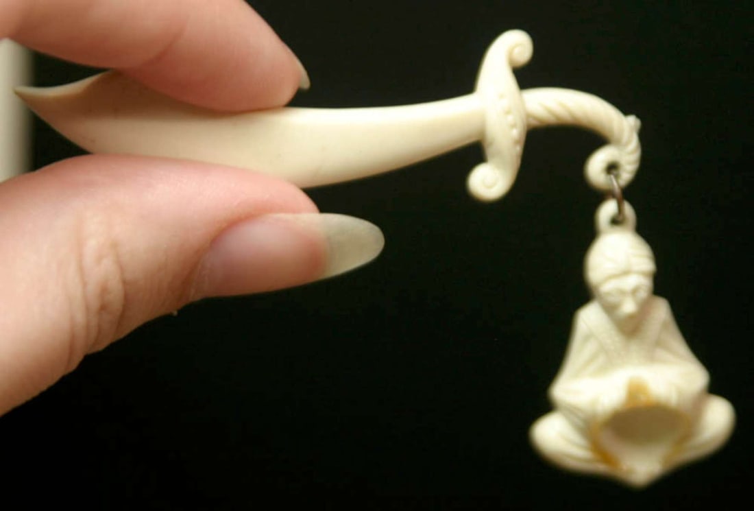 vintage estate jewelry: celluloid pin brooch: vintage bone colored (likely celluloid) sword shaped pin with dangly part shaped like a man in a robe (Saint? Buddha?)