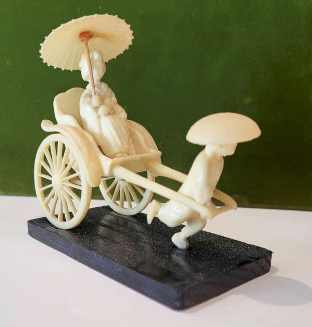 vintage celluloid Asian grouping: celluloid antique or vintage statue depicting a boy pulling a Japenese (Geisha?) woman with a sun umbrella sitting on a rickshaw, on a wooden base