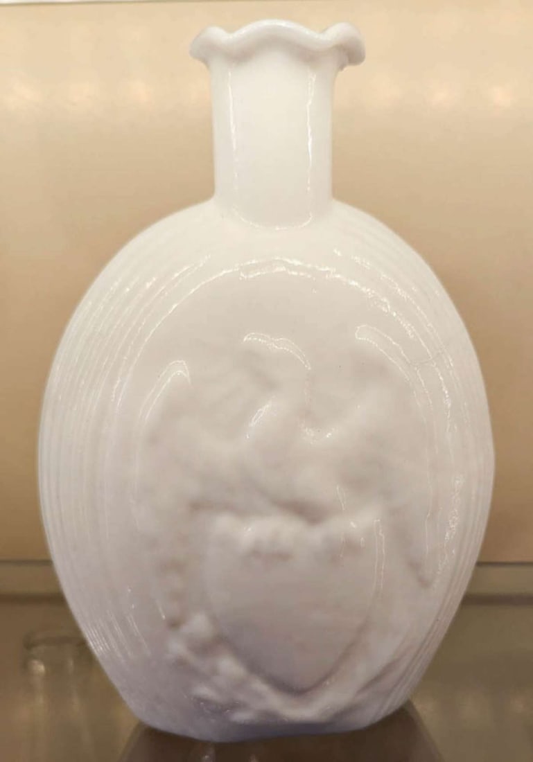 vintage or antique colored glass bottle: patriotic milk glass liquor bottle or flask with an Eagle with spread wings and sitting on a shield and an American flag on the reverse side with illegible wording