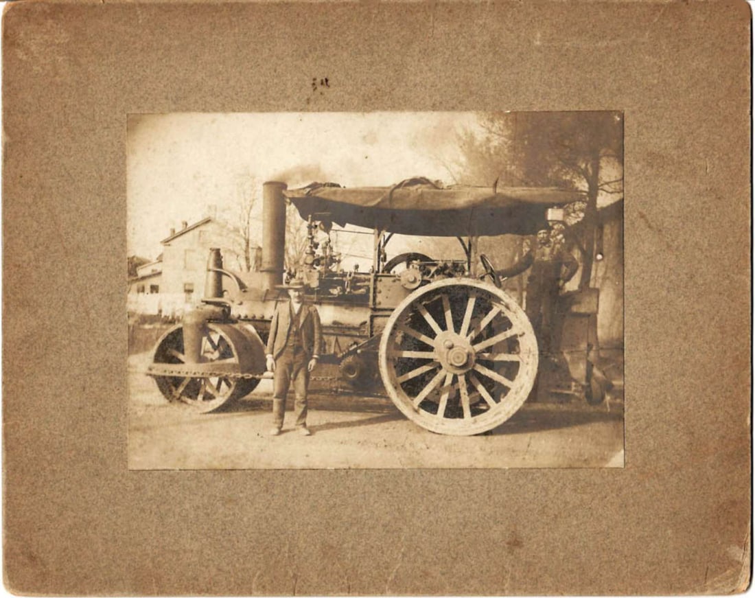 antique mounted photograph of a steam tractor with a roller: This is a circa 1892 mounted sepia photograph of some kind of steam tractor with a roller mounted in front, either for farming or constructing roads. According to the information on the back it 