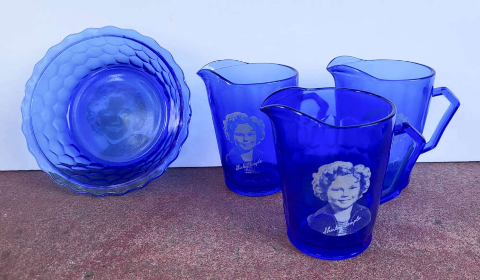 antique glass Shirley Temple set: antique glassware set, likely by Hazel Atlas in Cobalt blue with white Shirley Temple portrait and in-decal signature, set consisting of 3 milk pitchers or cereal pourers and a bowl or dis