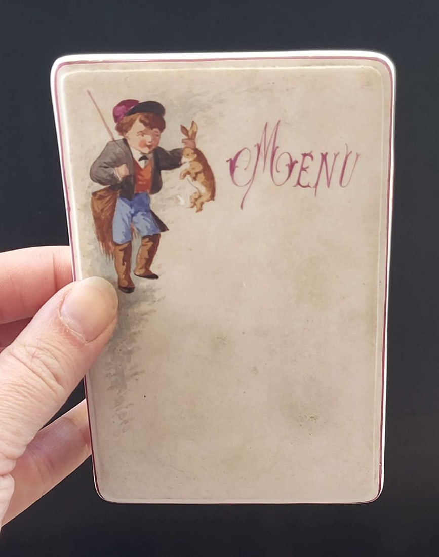 antique porcelain menu holder hunting theme: unmarked but likely English or French made table top standing menu shaped like a card stand and with hand painted image of a boy holding a bunny rabbit he just trapped or shot