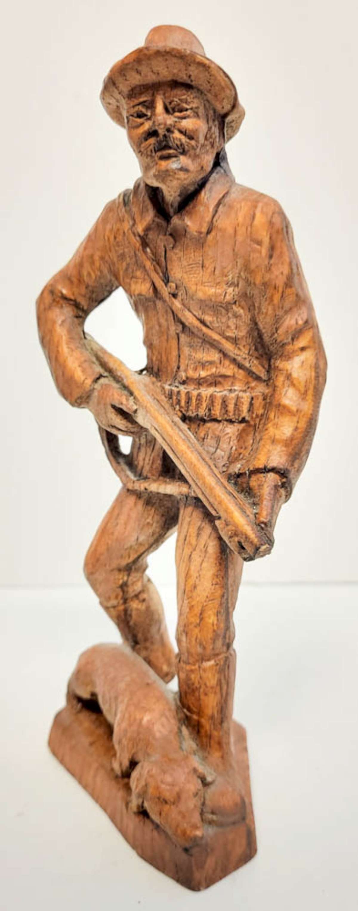 vintage carved wooden hunter sculpture: unsigned by the artist, this is a vintage carved wooden statue shaped like a man in hunting gear/clothing holding a shotgun or other weapon and with a dog laying at his feet