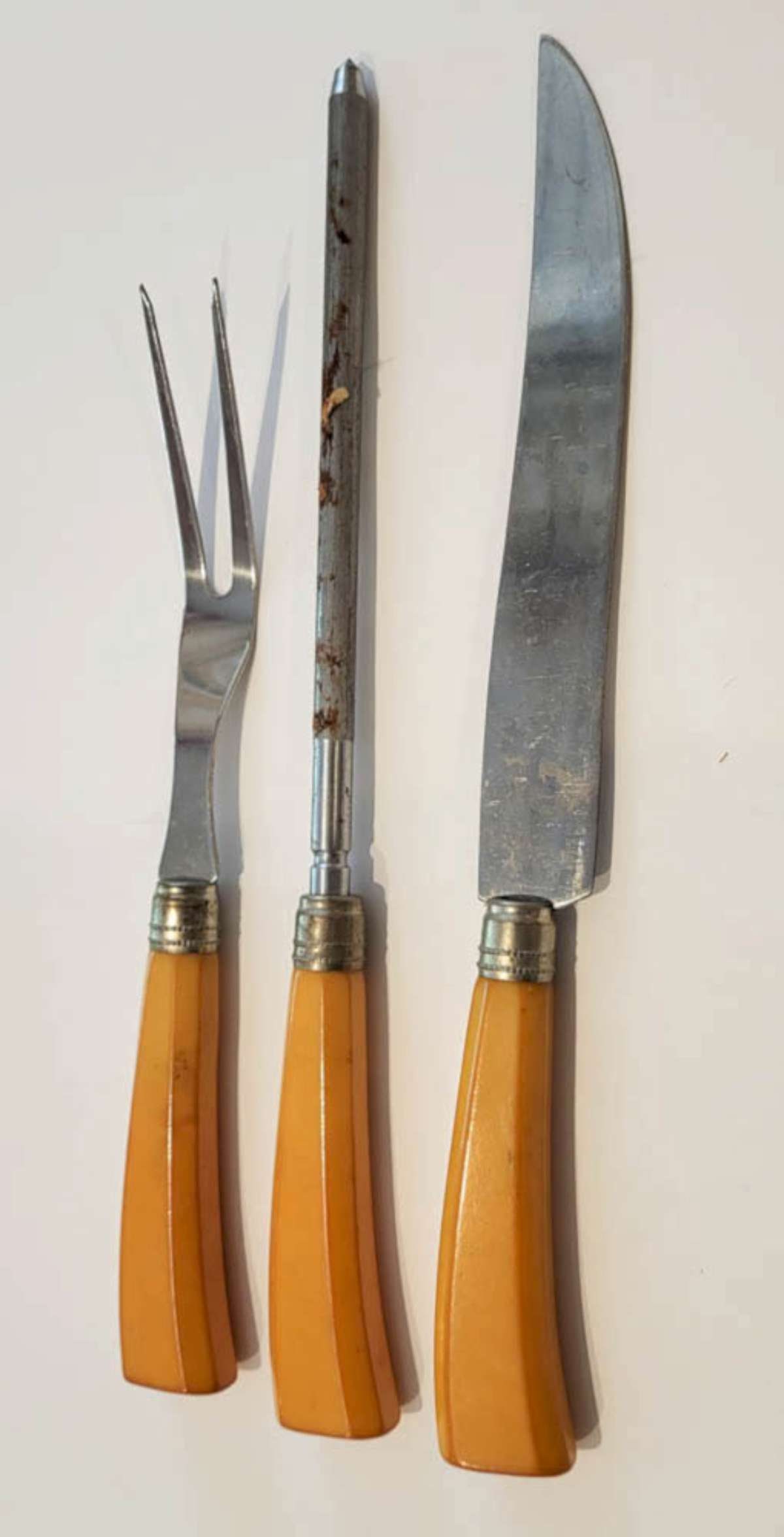 vintage Bakelite handled serving set: antique Art Deco Era cutlery or flatware set consisting of a knife sharpener, meat fork and meat slicing knife, each with Butterscotch colored Bakelite handle and marked Stainless Steel