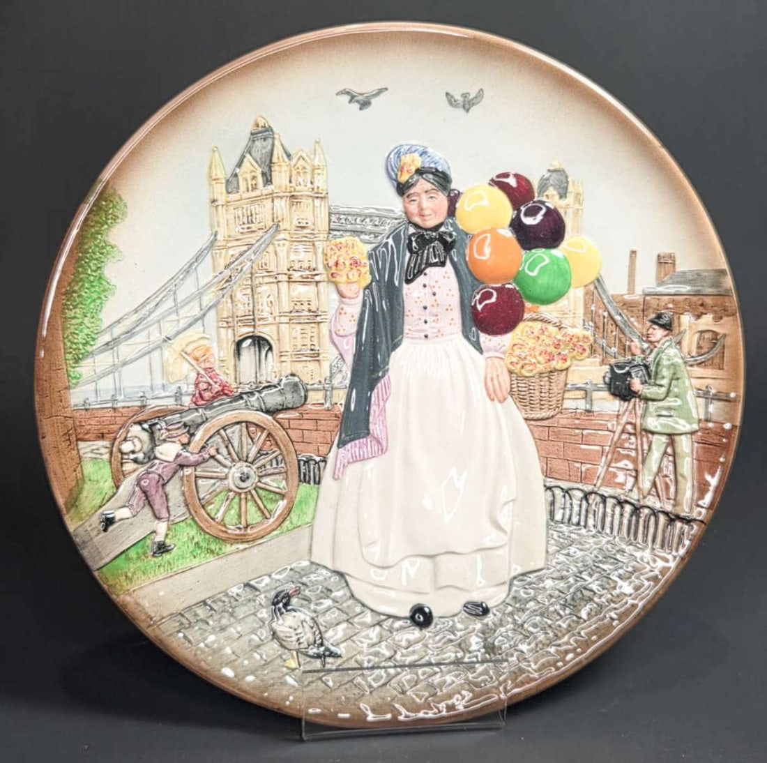 vintage Royal Doulton figural plate: vintage figural platter or large plate with 3-D design depicting a lady or woman walking around a street scene with pigeons selling colorful balloons, marked as shown underneath Royal Doulton Bi