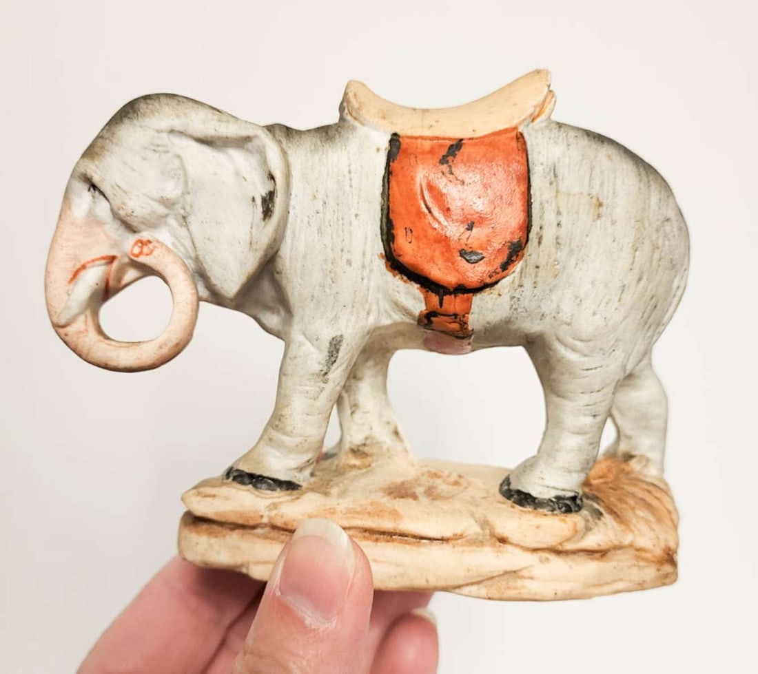 vintage bisque animal coin bank: adorable vintage or antique porcelain or bisque hand painted coin bank shaped like an elephant drinking or eating and with a saddle on his back, unmarked