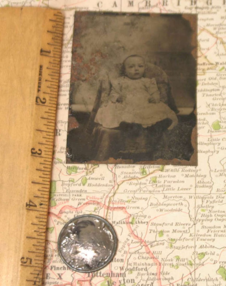 pair antique tintype photographs: first a mounted in metal frame (for use as a jewelry pendant?) portrait photograph of a young man, the second a black and white tintype of a toddler (girl or boy) in a white dress, sitting