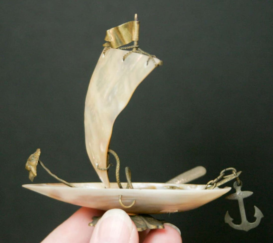 antique French MOP quelque chose ship: small antique mother of pearl and brass quelque chose object, shaped like a sailboat with flag, rudder, anchor and even a lion's face shaped figurehead, set on a base&comm