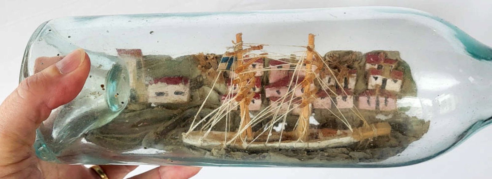 antique seascape Finland ship in a bottle: 1800's Primitive or Folk Art built and painted scene of a Scandinavian vessel with masts sailing in a harbor along the shoreline with houses, Finnish flag, whole piece in a very light
