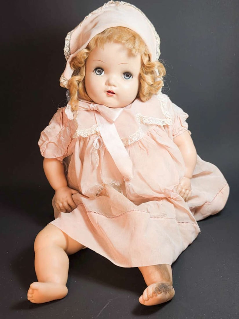 vintage composition head baby doll: girl with rubber limbs, pink and white dress, blonde curly hair, blue sleepy eyes and open mouth with teeth showing, with an extra dress (in better condition than the one she&a