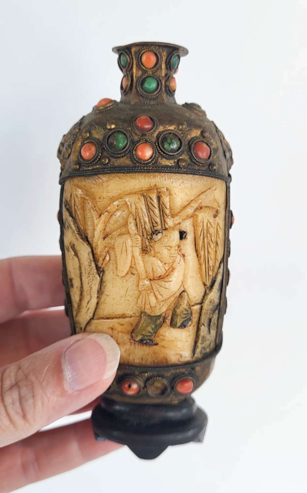 antique Asian snuff bottle: antique likely Chinese snuff bottle with gilt metal (coin silver?) and carved bone with girl design and cabochon inlaid stones (Coral, Jade and Malachite) and set on a wooden base
