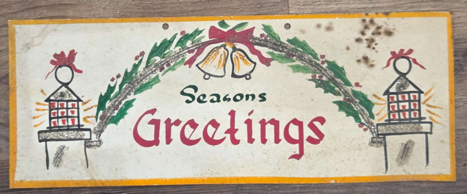 antique General store display Holiday sign: heavy cardstock with yellow edge and hand painted and glitter Holly, bells and an arch with burning candles in lanterns, great Christmas retail store piece reading Seasons Greentings