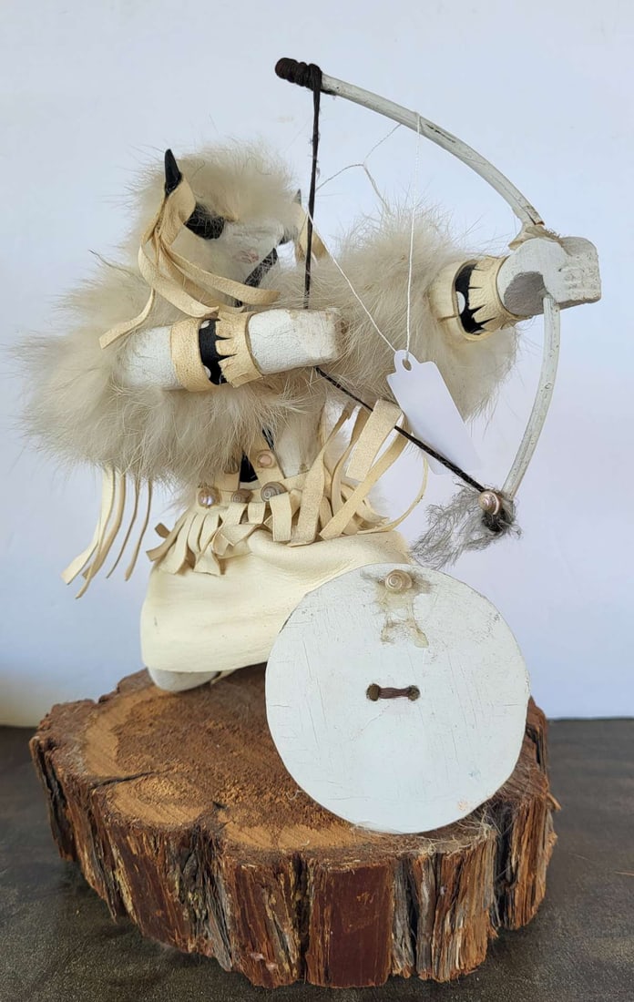 vintage signed Kachina Warrior doll: vintage Native American Indian made Kachina doll on a cut tree stump with carved wood, fabric and white fur, depicting a man with a shield and bow, titled Buffalo Warrior and illegib