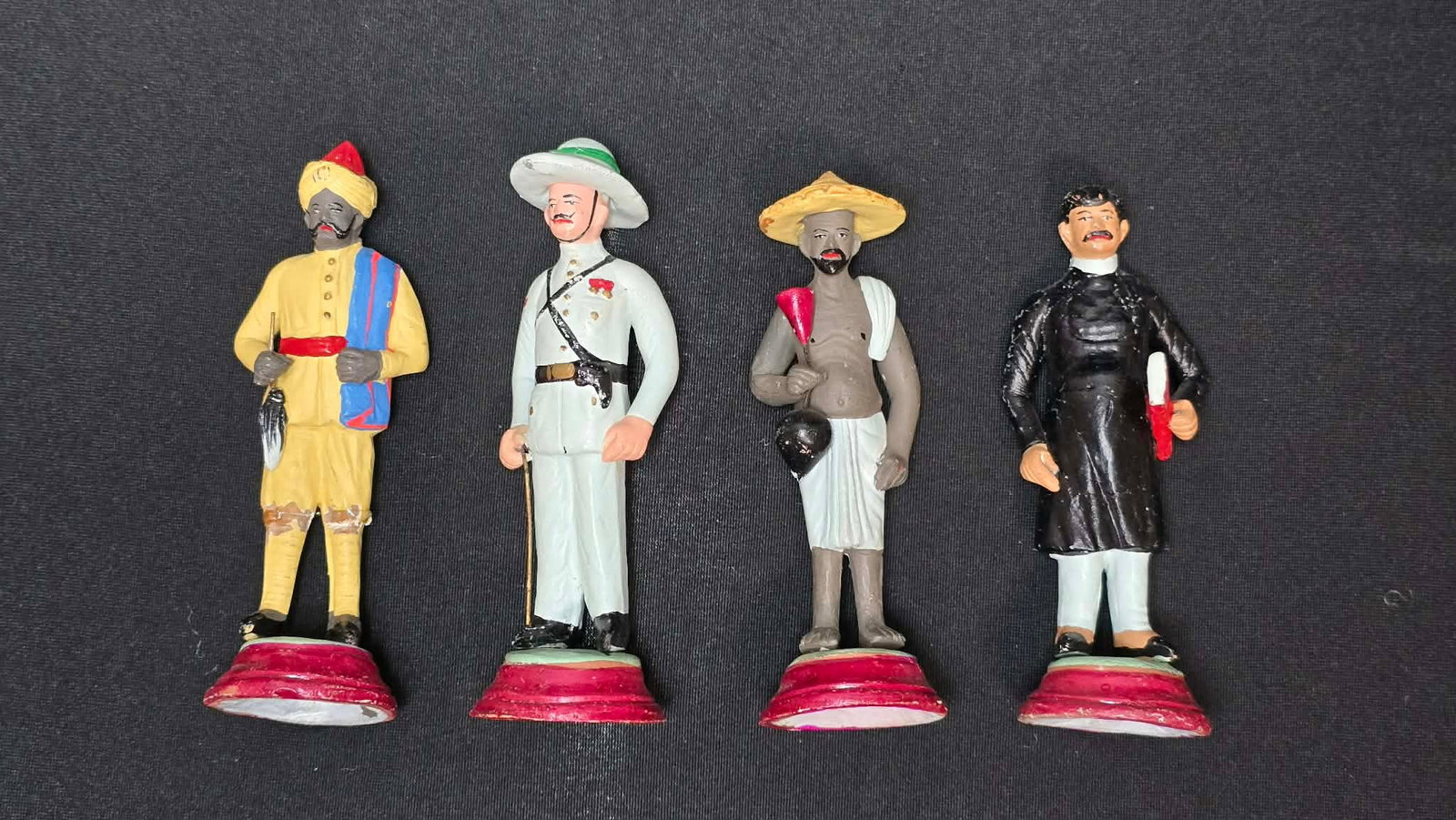 Set of Four Painted Figurines Representing Cultural & Occupational Characters: A group of four painted figurines depicting various cultural and occupational figures, each standing on a round base. Likely made of cast composition or plaster with hand-painted details, these figure