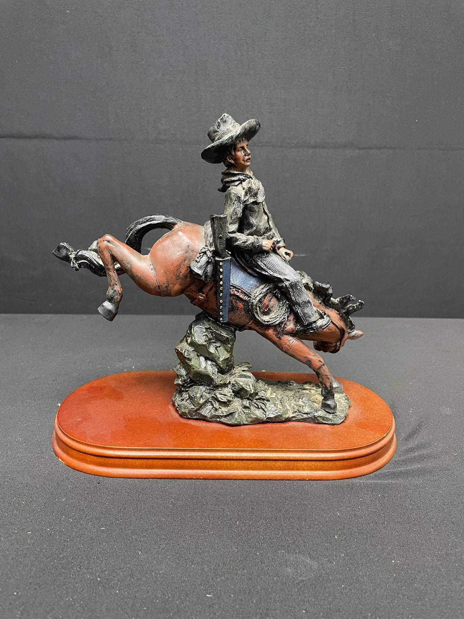 Resin Bronco Rider Sculpture: Resin sculpture on a polished wooden base of a bucking bronco rider done in the style of Frederic Remington.