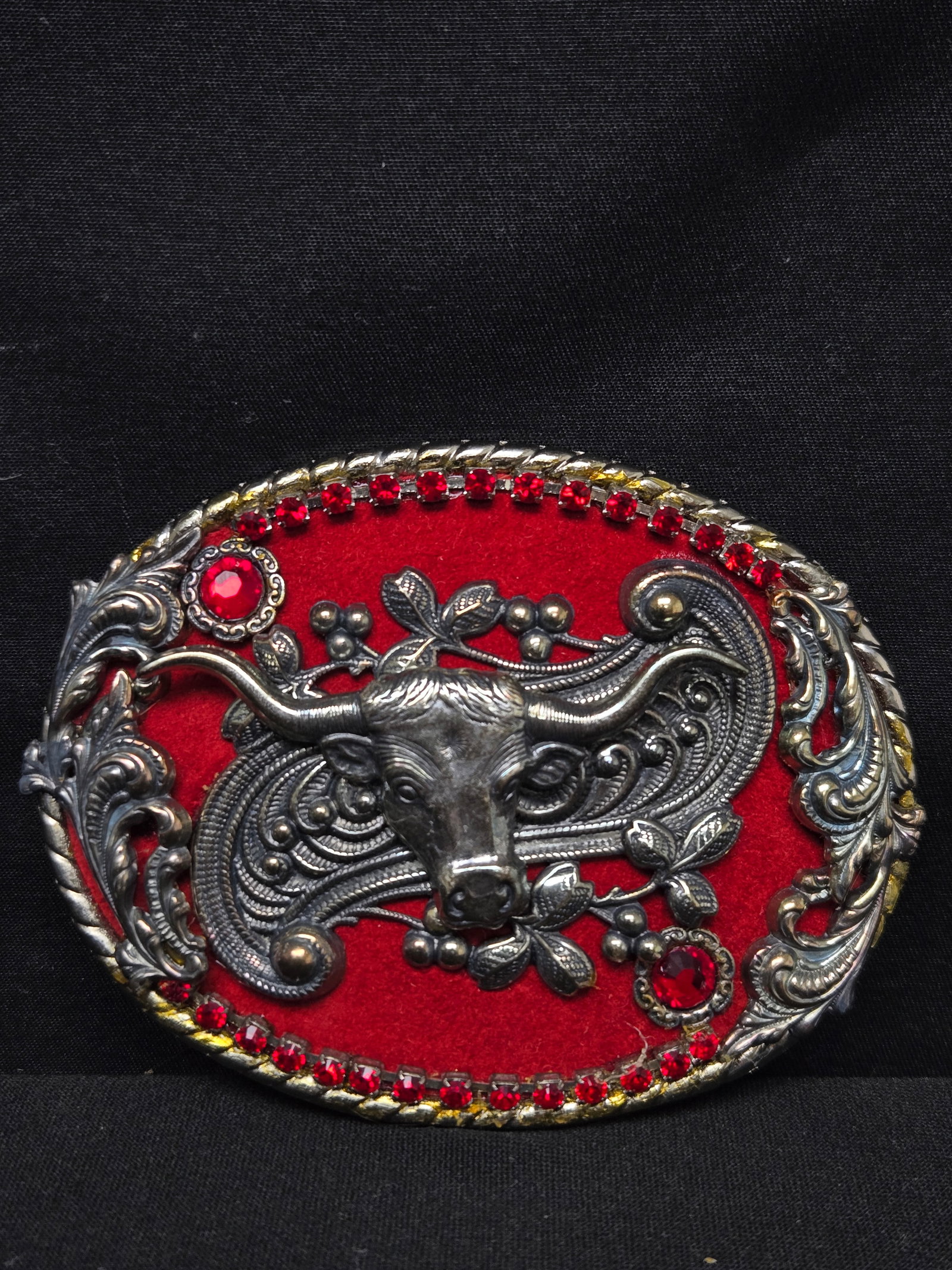 Red Decorative Longhorn Belt Buckle: Decorative belt buckle with red fabric background and a silver longhorn in the center. Decorated with red rhinestones and silver fleur de lis.