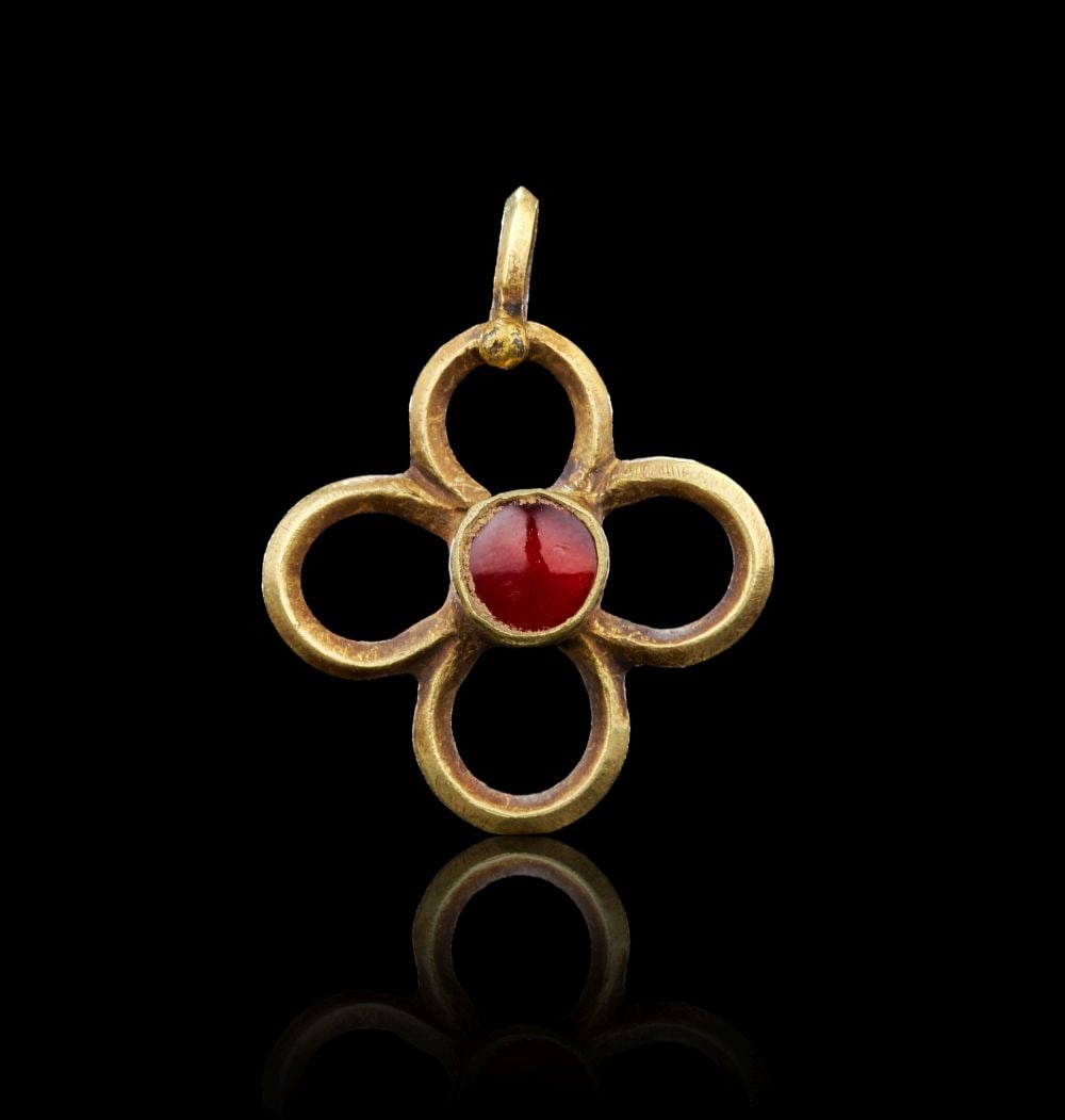 A BYZANTINE GOLD AND GARNET CROSS CIRCA 6TH CENTURY A.D.: Lot 117. A BYZANTINE GOLD AND GARNET CROSS Circa 6th Century A.D. Fashioned from gold, this openwork cross is composed of four rounded arms forming a symmetrical quatrefoil shape. At the centre, a ci