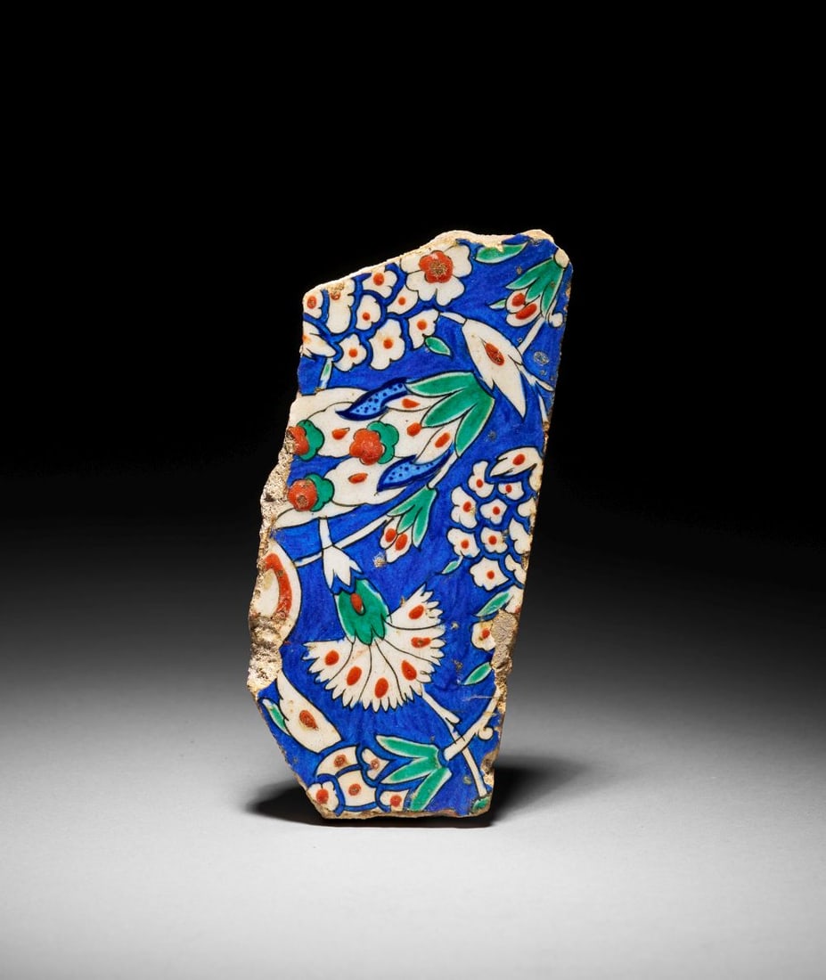 AN IZNIK POTTERY TILE FRAGMENT OTTOMAN TURKEY, CIRCA 1580: Lot 7. AN IZNIK POTTERY TILE FRAGMENT Ottoman Turkey, Circa 1580 Composed of fritware with a brilliant transparent glaze, this fragment preserves part of a densely painted floral composition characte