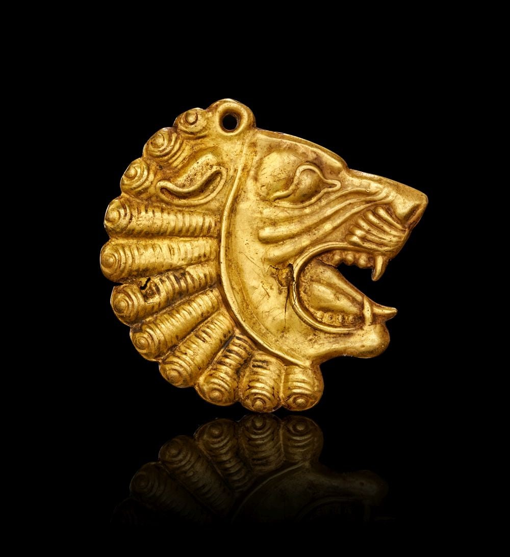 ACHAEMENID GOLD LION INLAY APPLIQUE, CIRCA 5TH CENTURY B.C.: ACHAEMENID GOLD LION INLAY APPLIQUÉ CIRCA 5TH CENTURY B.C. This finely worked gold appliqué is formed in the shape of a striding lion’s head shown in bold profile, its jaws open i