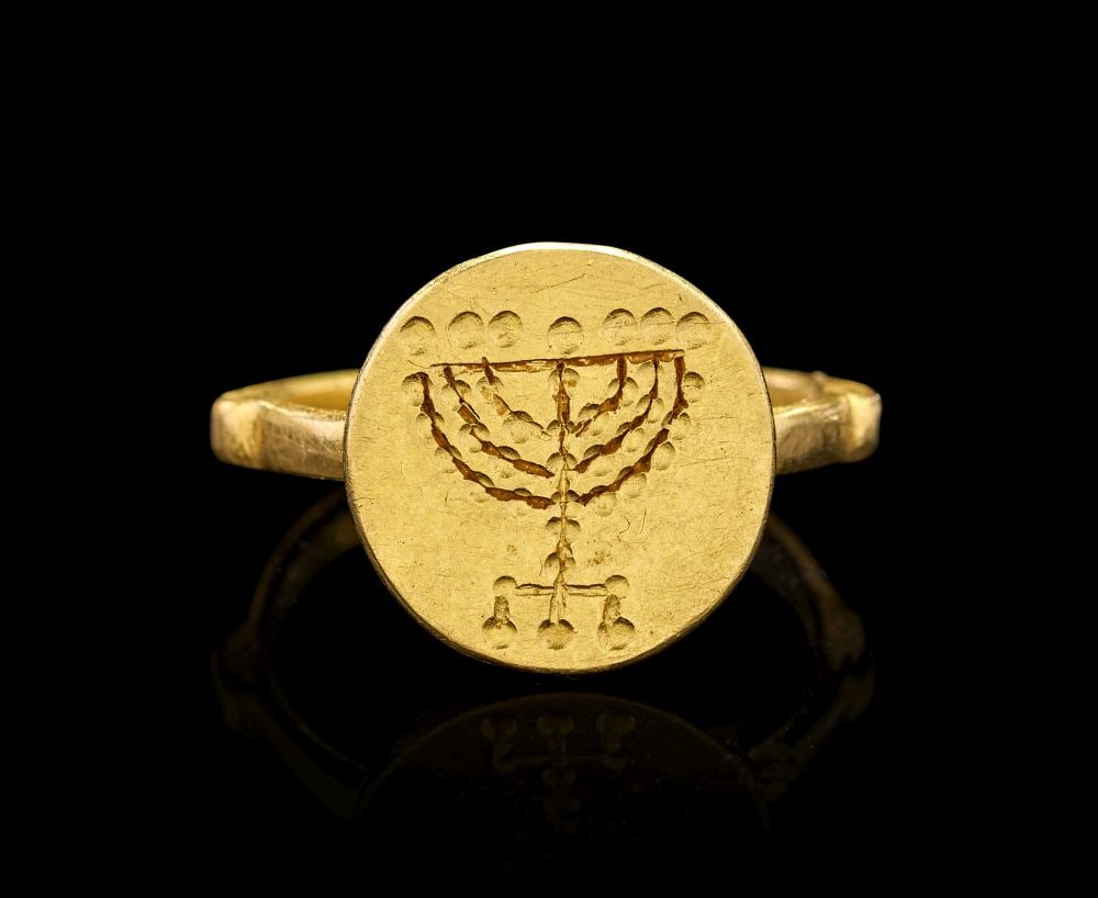 AN EARLY JEWISH GOLD ""MENORAH"" FINGER RING CIRCA 4TH-5TH CENTURY A.D.: AN EARLY JEWISH GOLD MENORAH FINGER RING, CIRCA 4TH–5TH CENTURY A.D. Of warm, softly lustrous gold, the ring is formed with a circular, flat bezel rising from a slender hoop, its proportions a
