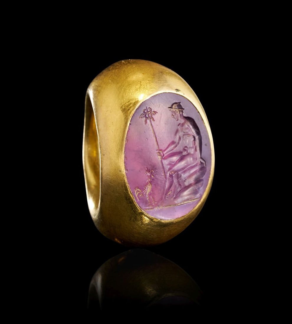 AN EXCEPTIONALROMAN AMETHYST INTAGLIO DEPICTING HERMES WITH A STAFF RESTING WITH A COCKEREL, CIRCA: AN EXCEPTIONAL ROMAN GOLD RING SET WITH AN AMETHYST INTAGLIO DEPICTING HERMES, CIRCA 2ND CENTURY A.D. An exceptional Roman gold ring of substantial, sculptural form, set with a finely engraved a