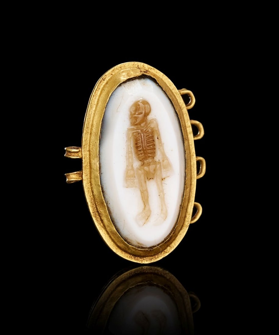 A ROMAN IMPERIAL BANDED AGATE CAMEO DEPICTING A STANDING SKELETON, CIRCA 2ND-3RD CENTURY A.D.: A ROMAN IMPERIAL BANDED AGATE CAMEO DEPICTING A STANDING SKELETON, CIRCA 2ND–3RD CENTURY A.D. Finely mounted in warm-toned gold, this Roman Imperial cameo is centred on an oval banded agate, e