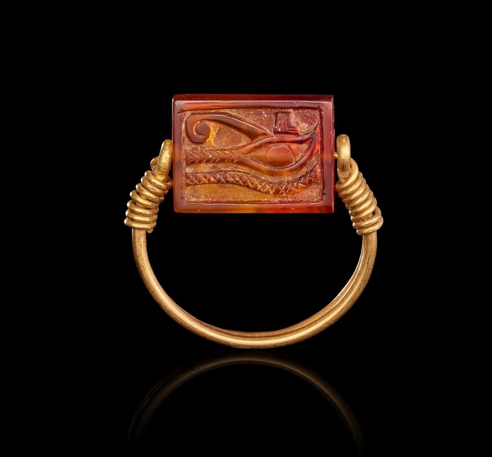 AN EGYPTIAN GOLD AND CARNELIAN SCARAB SWIVEL RING NEW KINGDOM, 19TH-20TH DYNASTY, CIRCA 1279: AN EGYPTIAN GOLD AND CARNELIAN SCARAB SWIVEL RING This finely preserved Egyptian swivel ring pairs warm gold with a richly coloured carnelian scarab, creating a jewel of both elegance and symbolic p