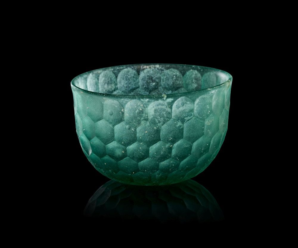 A SASANIAN FACET-CUT GLASS BOWL CIRCA 4TH-6TH CENTURY A.D.: A SASANIAN FACET-CUT GLASS BOWL CIRCA 4TH–6TH CENTURY A.D. This elegant Sasanian glass bowl is a refined example of late antique luxury glass, distinguished by its carefully cut honeycomb patte
