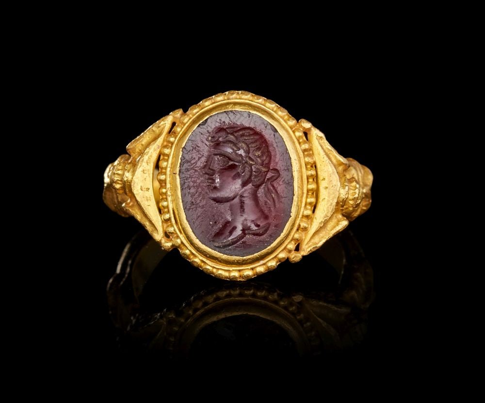 A ROMAN GOLD & GARNET INTAGLIO BUST OF AN EMPRESS, CIRCA 1ST-2ND CENTURY A.D.: A ROMAN GOLD AND GARNET INTAGLIO RING WITH A BUST OF AN EMPRESS, CIRCA 1ST–2ND CENTURY A.D. A finely-modelled Roman gold finger-ring, centred by an oval garnet intaglio engrave