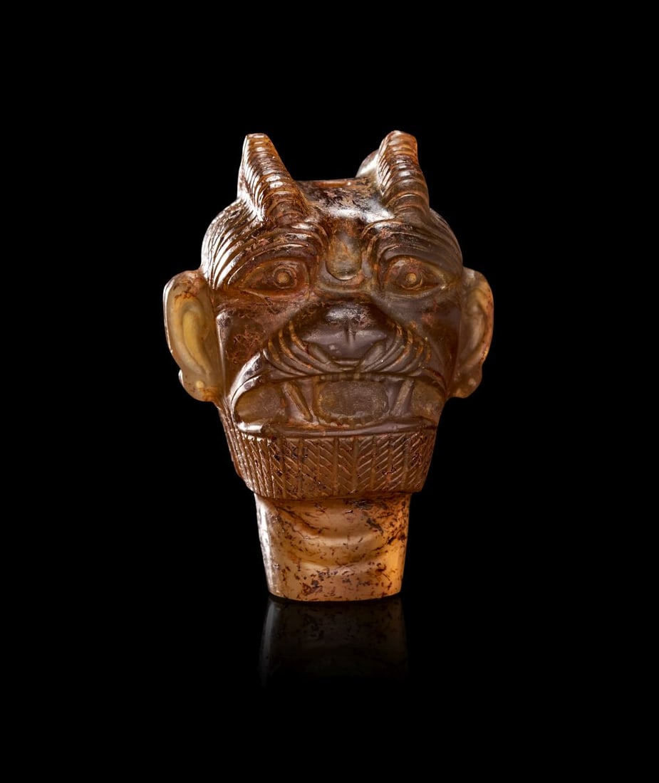 A NEO-ASSYRIAN CHALCEDONY HEAD OF PAZUZU CIRCA 8TH-7TH CENTURY B.C.: A NEO-ASSYRIAN CHALCEDONY HEAD OF PAZUZU, CIRCA 8TH–7TH CENTURY B.C. Carved from a richly variegated chalcedony of warm honey and umber tones, this compelling head of Pazuzu em