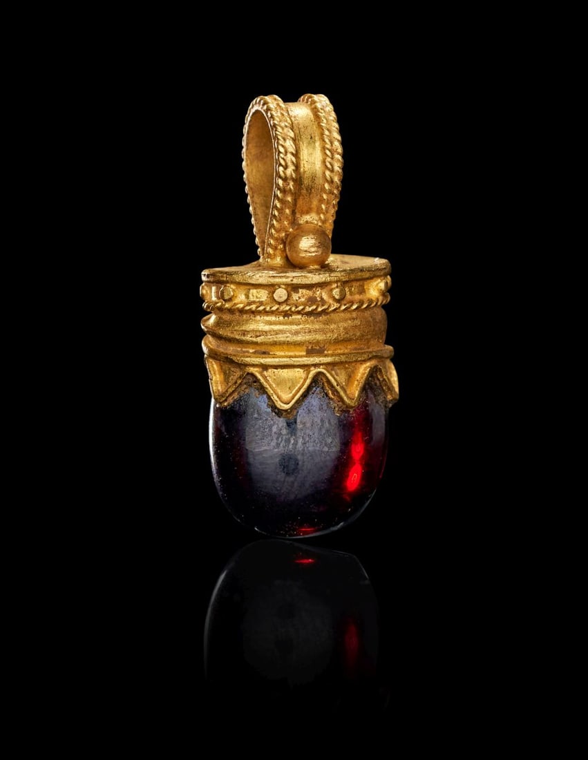 A ROMAN GOLD & GARNET AMULET, CIRCA 1ST-2ND CENTURY A.D.: A ROMAN GOLD & GARNET AMULET, CIRCA 1ST–2ND CENTURY A.D. Finely wrought in warm, high-karat gold, this Roman amulet is centred on a deep red garnet of rounded, gently tapering form, its ri