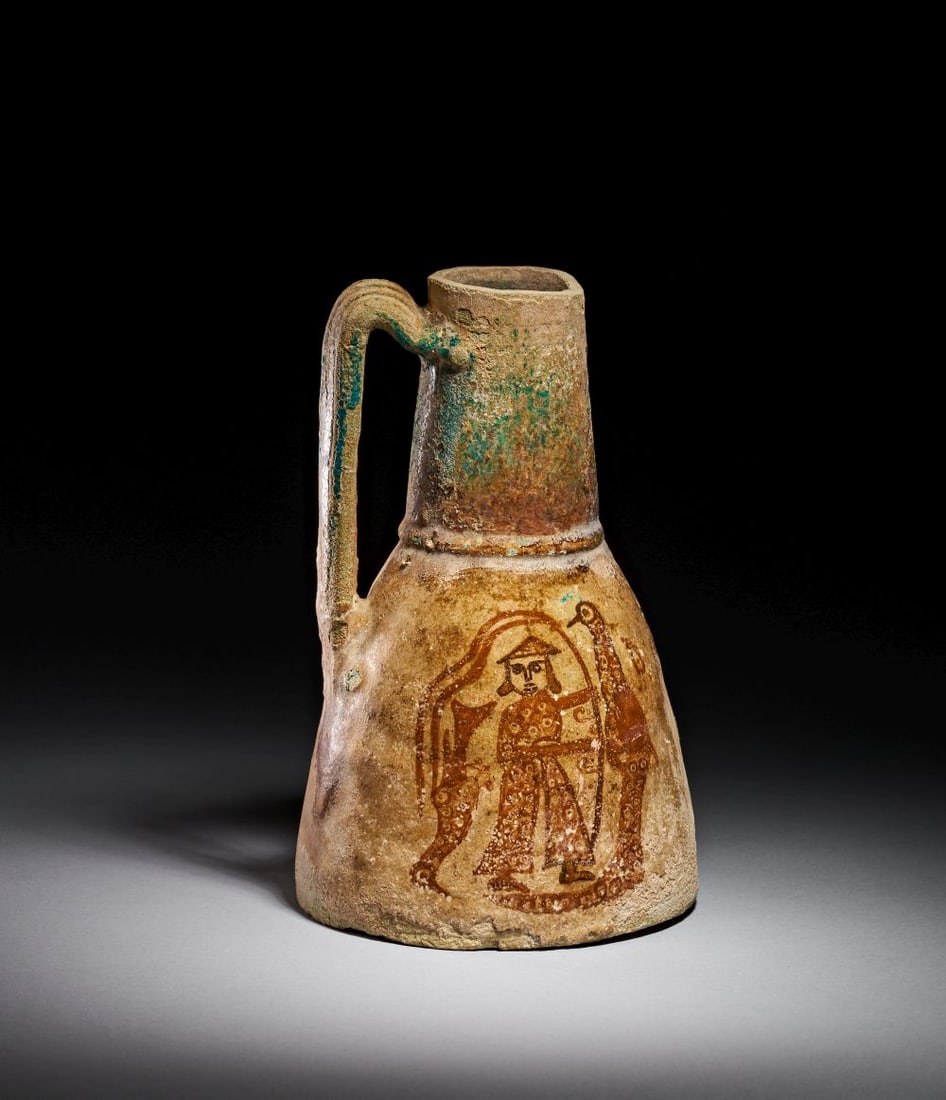 A CERAMIC EWER DEPICTING A MAN WITH A PEACOCK, PROBABLY MIDDLE AGES: A MEDIEVAL GLAZED CERAMIC EWER WITH FIGURAL DECORATION, CIRCA 12TH–14TH CENTURY A.D. Modelled in ceramic and enlivened with a lustrous glaze, this handsome ewer is formed with a broad, gently