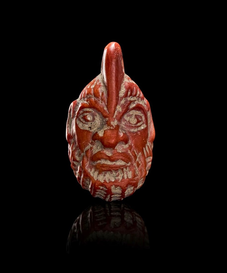 A WESTERN ASIATIC JASPER HEAD AMULET, CIRCA 7TH CENTURY B.C.: A WESTERN ASIATIC JASPER HEAD AMULET, CIRCA 7TH CENTURY B.C. Carved in deep red jasper of compact, weighty substance, this striking head amulet presents a powerfully stylised male visage crowned by