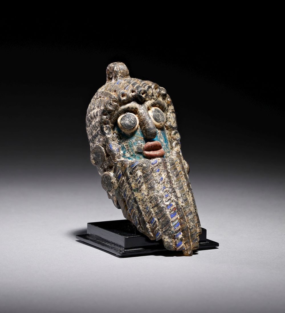 A PHOENICIAN GLASS BEARDED HEAD BEAD CIRCA 5TH-4TH CENTURY B.C.: A PHOENICIAN GLASS BEARDED HEAD BEAD CIRCA 5TH-4TH CENTURY B.C.A striking Phoenician glass bead formed as a miniature bearded head, modelled in the round with a powerful, mask-like presence. The compa