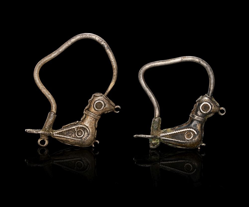 TWO ROMAN SILVER DOVE EARRINGS, CIRCA 1ST-2ND CENTURY A.D.: TWO ROMAN SILVER DOVE EARRINGS, CIRCA 1ST–2ND CENTURY A.D. Silver, finely cast and delicately worked, each earring formed as a stylised dove perched in profile, the compact body swelling gentl