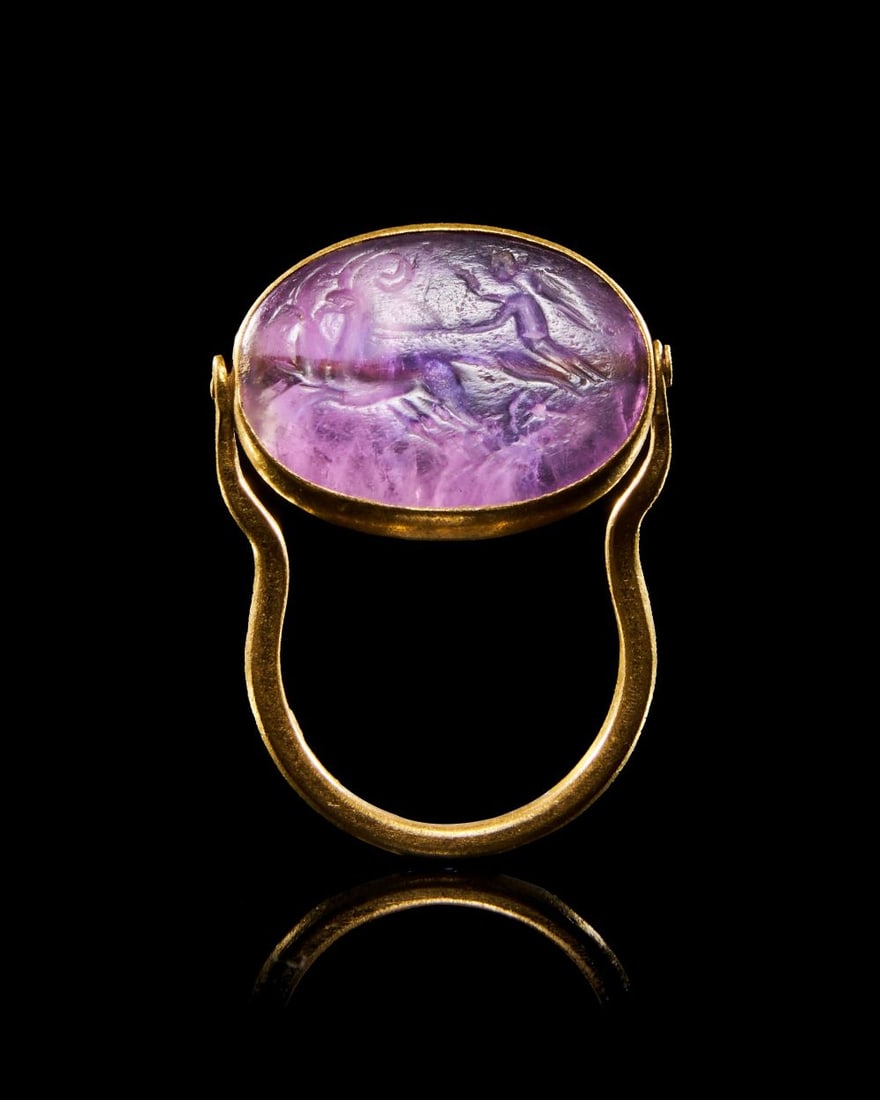 A ROMAN AMETHYST RING STONE DEPICTING CHARIOT RACING SCENE, CIRCA 2ND CENTURY A.D.: A ROMAN AMETHYST RING STONE DEPICTING CHARIOT RACING SCENE, CIRCA 2ND CENTURY A.D. An oval amethyst i