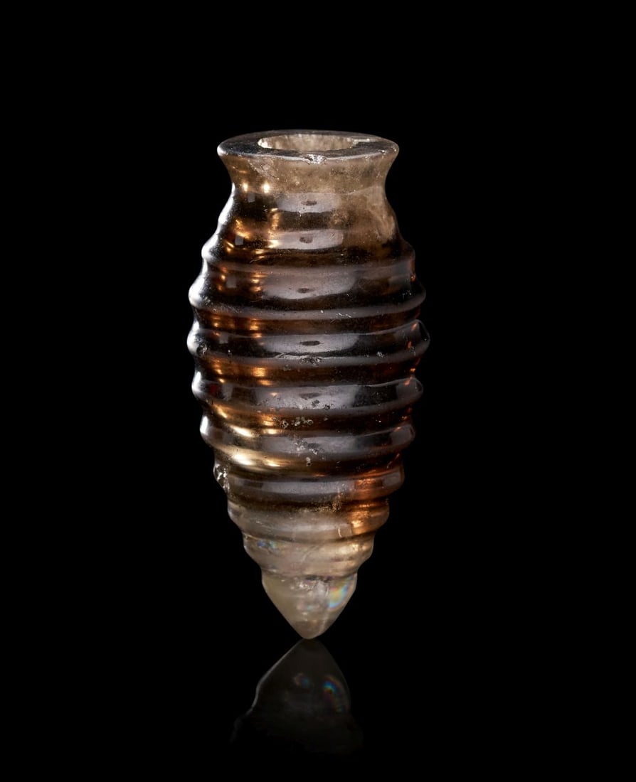 A FATIMID BROWN CRYSTAL COSMETIC VESSEL, CIRCA 10TH CENTURY, EGYPT: A FATIMID BROWN CRYSTAL COSMETIC VESSEL, CIRCA 10TH CENTURY, EGYPT Of tapering cylindrical form, this finely carved brown crystal cosmetic vessel narrows gently towards a pointed base, rising to a s