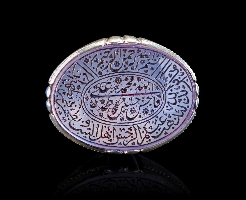 A CALLIGRAPHIC INSCRIBED AGATE RING, 19TH CENTURY, PERSIA: A CALLIGRAPHIC INSCRIBED AGATE RING, 19TH CENTURY, PERSIA This impressive agate ring is set with a large oval stone of soft lavender-grey hue, finely engraved in intaglio with an intricate calligrap