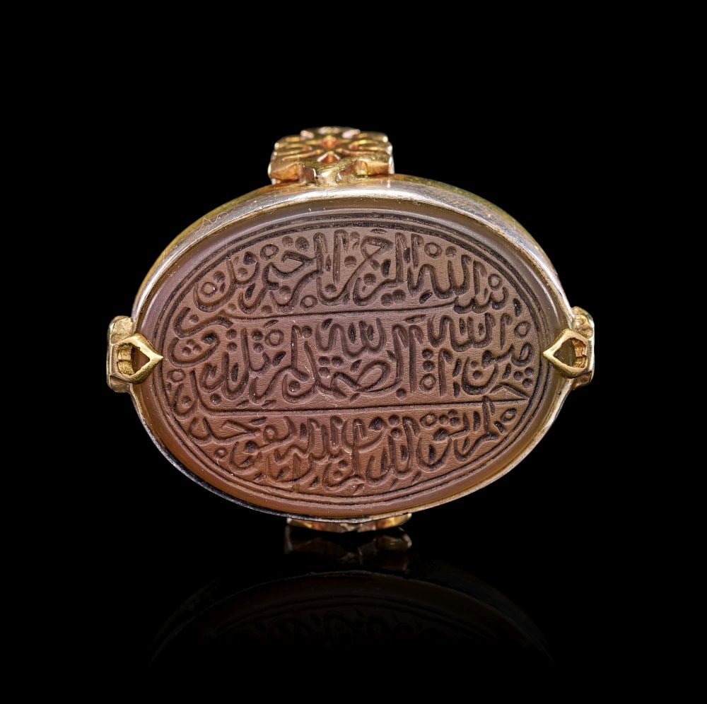 A CALLIGRAPHIC INSCRIBED AGATE RING, 19TH CENTURY, PERSIA: A CALLIGRAPHIC INSCRIBED AGATE RING, 19TH CENTURY, PERSIA This impressive 19th-century Persian ring centres on a large oval agate of rich, earthy brown hue, its surface deeply carved with an elegant