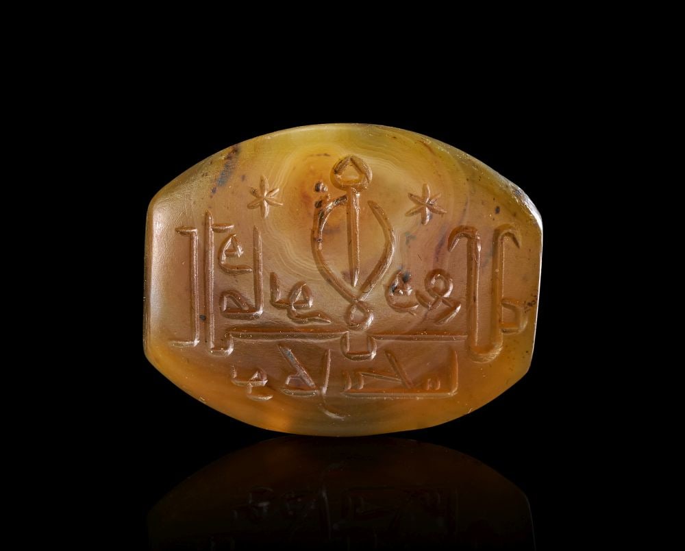A CALLIGRAPHIC INSCRIBED AGATE BEAD, 19TH CENTURY, PERSIA: A CALLIGRAPHIC INSCRIBED AGATE BEAD, 19TH CENTURY, PERSIA This 19th-century Persian agate bead is carved from a warm honey-brown stone of softly mottled translucency. The oval face is engraved in in